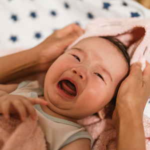 Photograph: crying infant being dried with pink towel by adult hands on star blanket