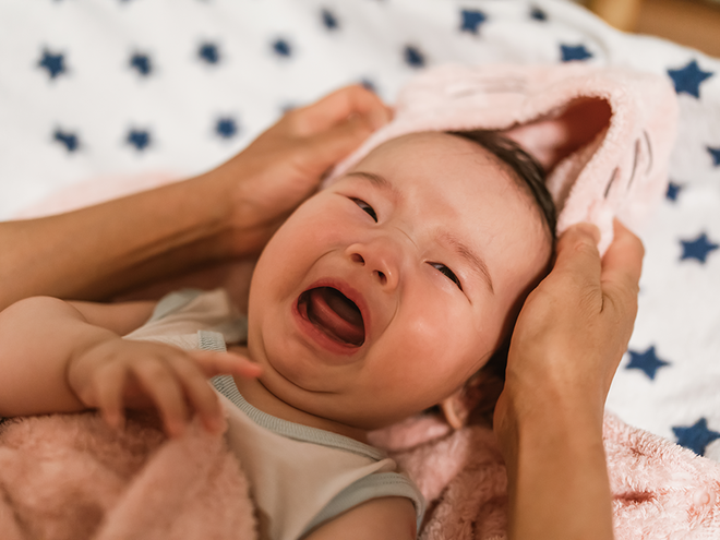 Photograph: crying infant being dried with pink towel by adult hands on star blanket