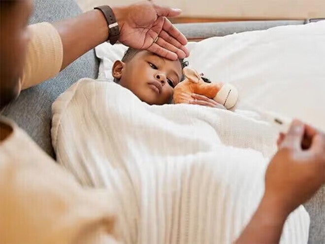 Ένα παιδί ξαπλωμένο με κουβέρτα και θερμόμετρο, φροντίζεται από ενήλικα.